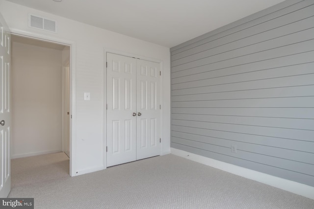 unfurnished bedroom featuring wood walls, a closet, and light colored carpet