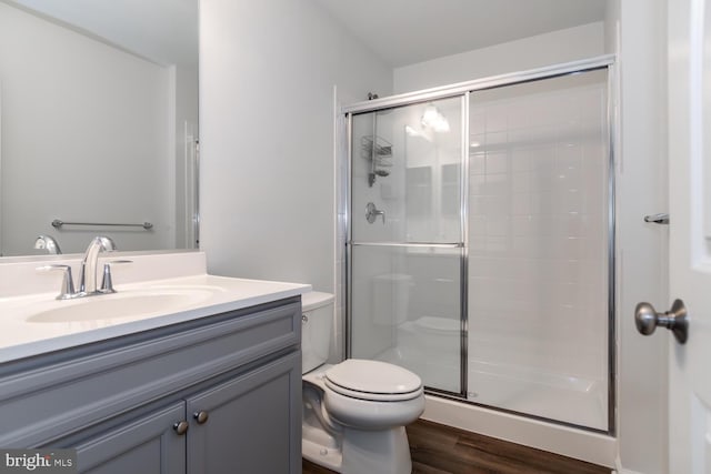 bathroom with wood-type flooring, vanity, toilet, and a shower with shower door