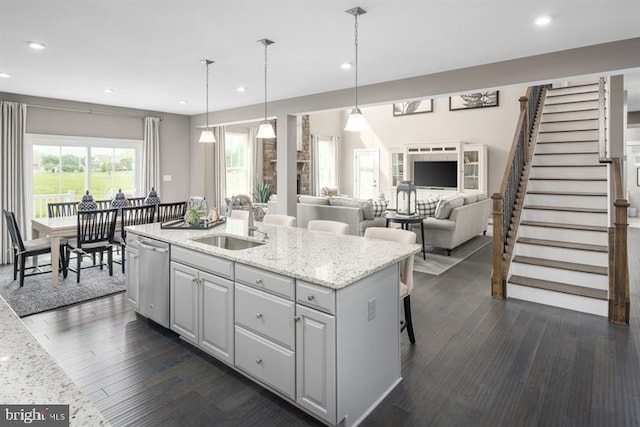 kitchen with light stone counters, sink, decorative light fixtures, a center island with sink, and dishwasher