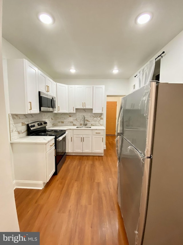 kitchen with decorative backsplash, appliances with stainless steel finishes, sink, light hardwood / wood-style floors, and white cabinetry