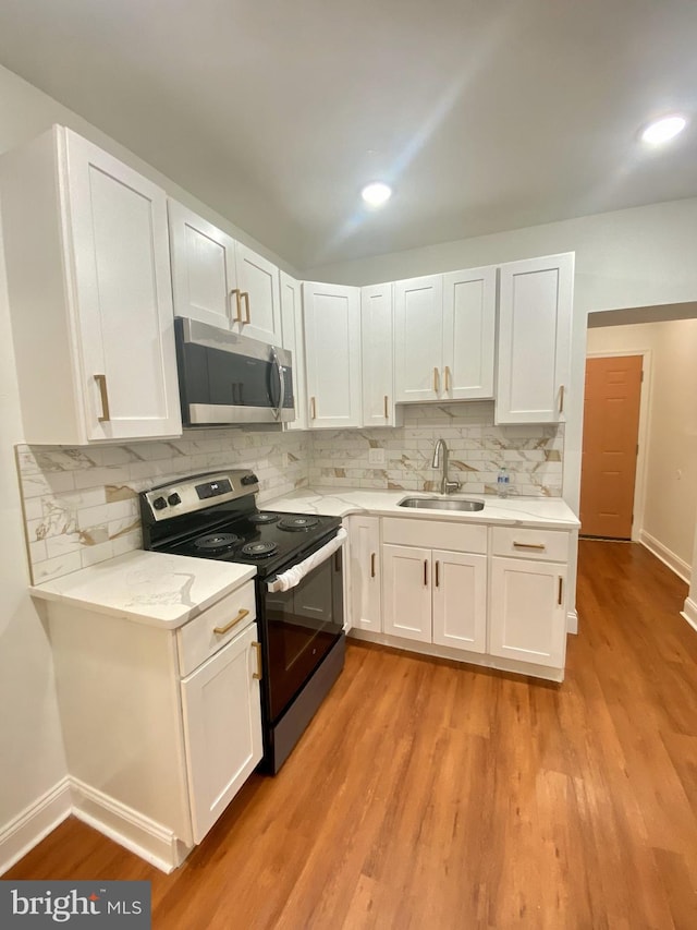 kitchen featuring light wood-type flooring, tasteful backsplash, sink, white cabinets, and black / electric stove