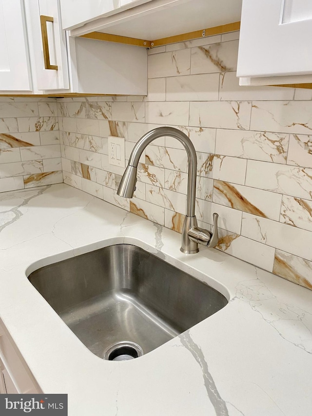 room details featuring white cabinets, decorative backsplash, light stone counters, and sink