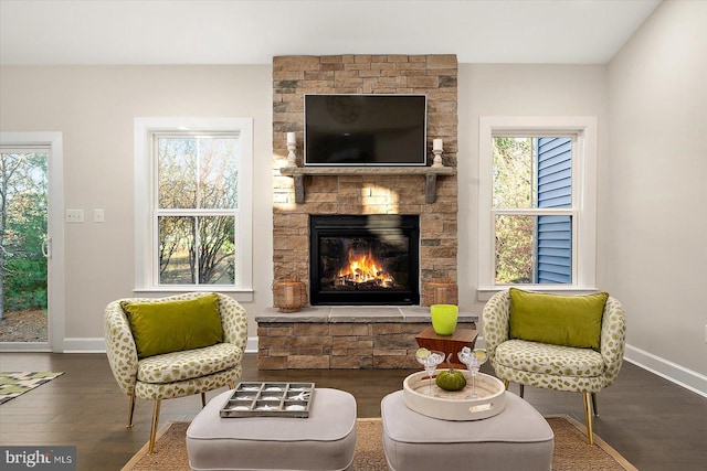 sitting room featuring dark wood-type flooring, a stone fireplace, and a healthy amount of sunlight