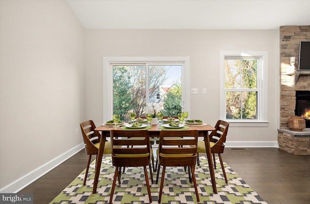 dining room with a stone fireplace, a wealth of natural light, and dark hardwood / wood-style floors