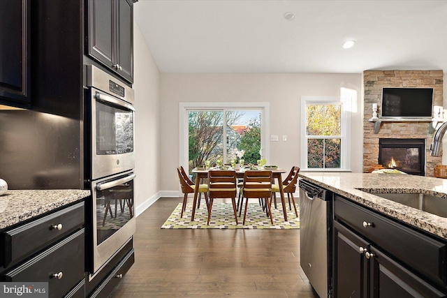 kitchen with light stone counters, a stone fireplace, dark wood-type flooring, and stainless steel appliances