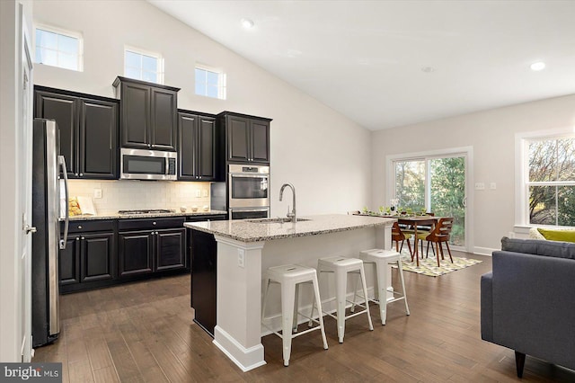 kitchen featuring sink, dark wood-type flooring, an island with sink, a kitchen bar, and appliances with stainless steel finishes