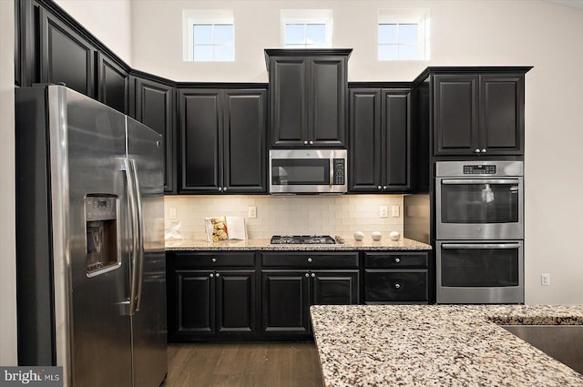 kitchen with light stone counters, stainless steel appliances, tasteful backsplash, and dark wood-type flooring