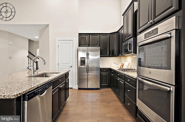 kitchen with a kitchen island with sink, sink, light stone countertops, light hardwood / wood-style floors, and stainless steel appliances