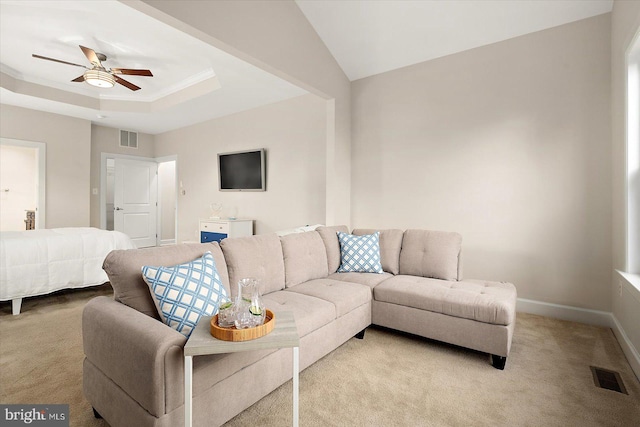 carpeted living room with a raised ceiling, ceiling fan, and crown molding