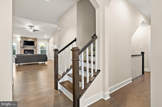 stairs featuring a fireplace, wood-type flooring, and ceiling fan