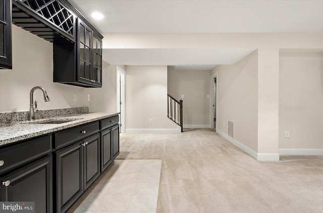 kitchen with sink, light stone counters, and light carpet