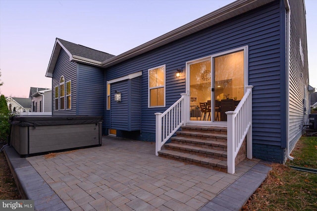 back house at dusk featuring a patio and a hot tub