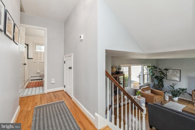 corridor with hardwood / wood-style floors, high vaulted ceiling, and a baseboard heating unit