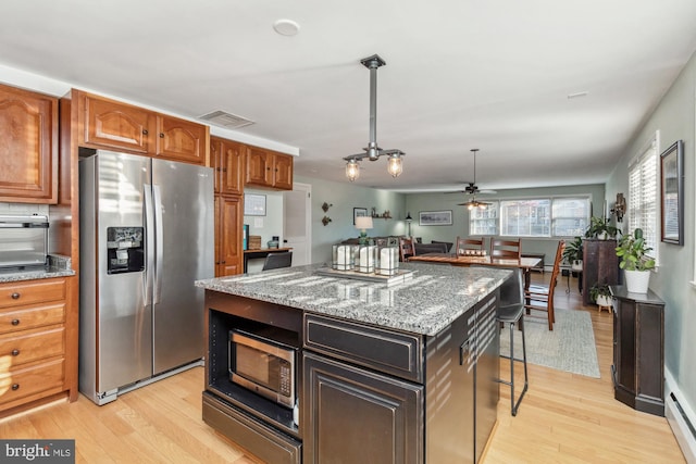 kitchen with appliances with stainless steel finishes, light wood-type flooring, light stone counters, pendant lighting, and a kitchen island