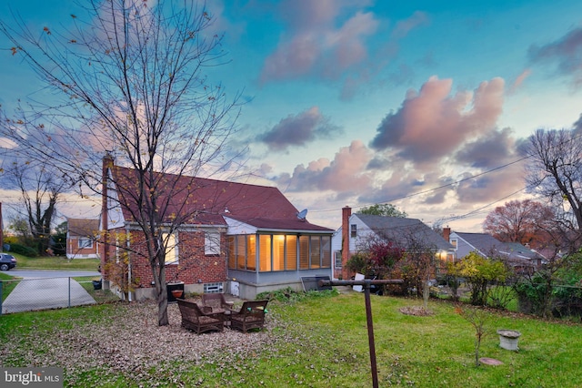 back house at dusk with a lawn and a sunroom