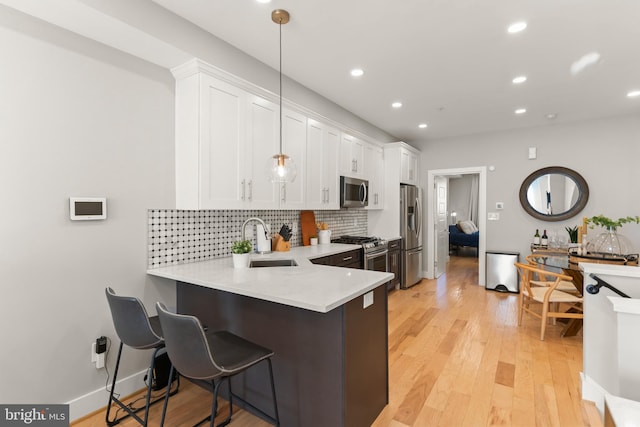 kitchen with white cabinetry, sink, light hardwood / wood-style flooring, kitchen peninsula, and appliances with stainless steel finishes