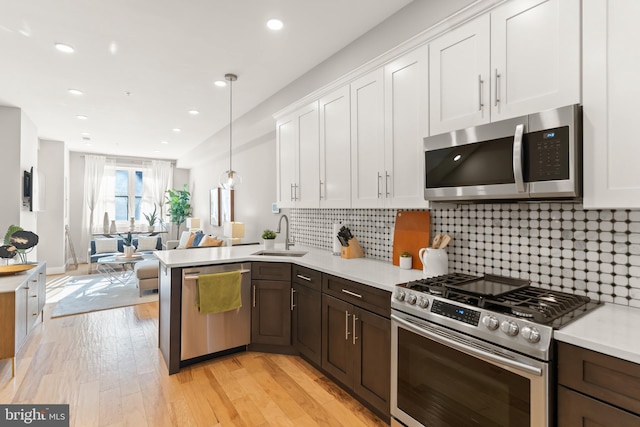 kitchen with stainless steel appliances, sink, light hardwood / wood-style flooring, white cabinets, and hanging light fixtures