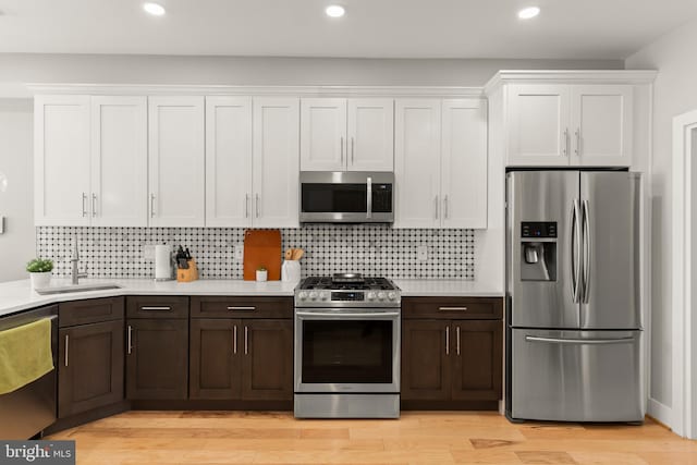 kitchen featuring sink, decorative backsplash, appliances with stainless steel finishes, light hardwood / wood-style floors, and white cabinetry