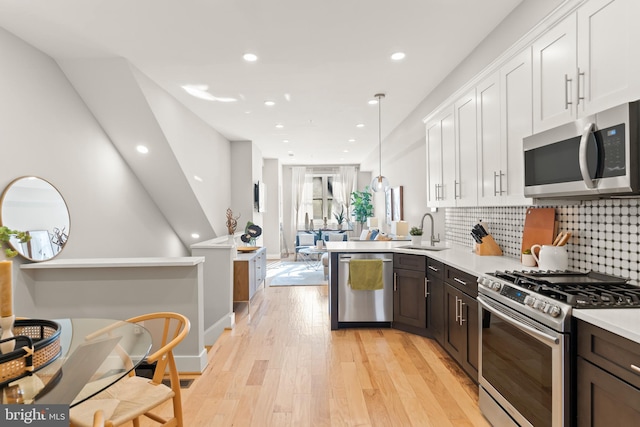 kitchen with kitchen peninsula, appliances with stainless steel finishes, sink, pendant lighting, and light hardwood / wood-style floors