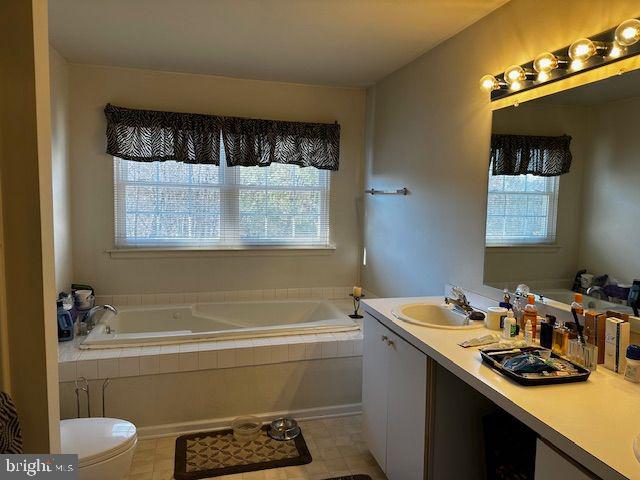 bathroom with vanity, toilet, and tiled tub