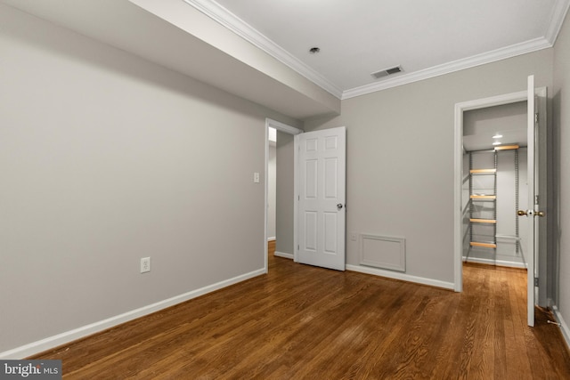 unfurnished bedroom featuring dark hardwood / wood-style floors, a walk in closet, and crown molding