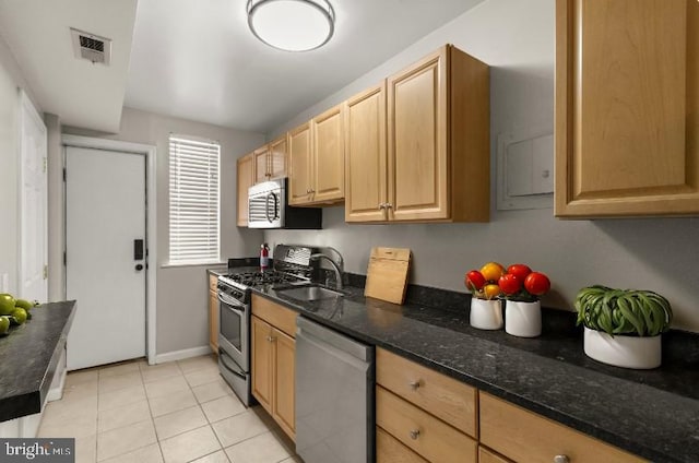 kitchen featuring light tile patterned flooring, sink, stainless steel appliances, and dark stone counters