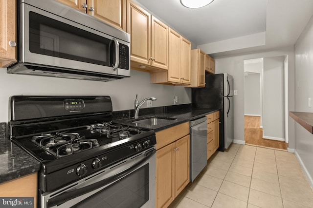 kitchen with appliances with stainless steel finishes, light tile patterned floors, dark stone counters, and sink