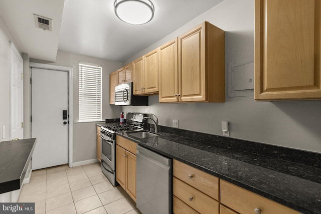 kitchen with sink, light tile patterned floors, stainless steel appliances, and dark stone counters