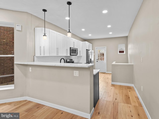 kitchen featuring kitchen peninsula, appliances with stainless steel finishes, white cabinets, and light hardwood / wood-style flooring