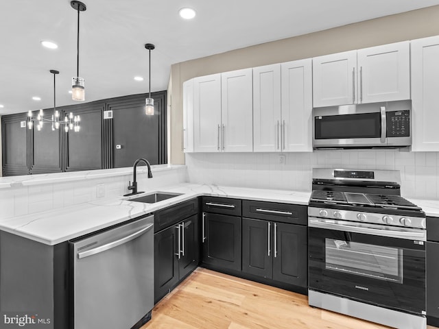 kitchen featuring white cabinets, sink, light wood-type flooring, decorative light fixtures, and stainless steel appliances