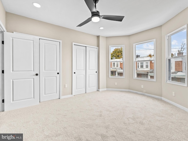 unfurnished bedroom featuring multiple closets, ceiling fan, and light colored carpet