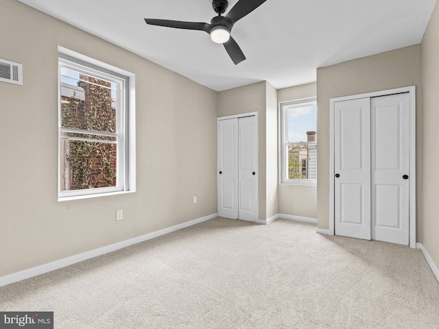 unfurnished bedroom with ceiling fan, light colored carpet, multiple closets, and multiple windows