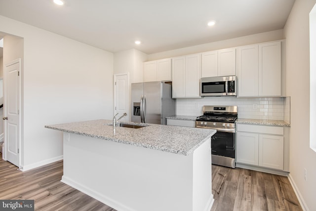 kitchen with light hardwood / wood-style floors, sink, appliances with stainless steel finishes, and an island with sink