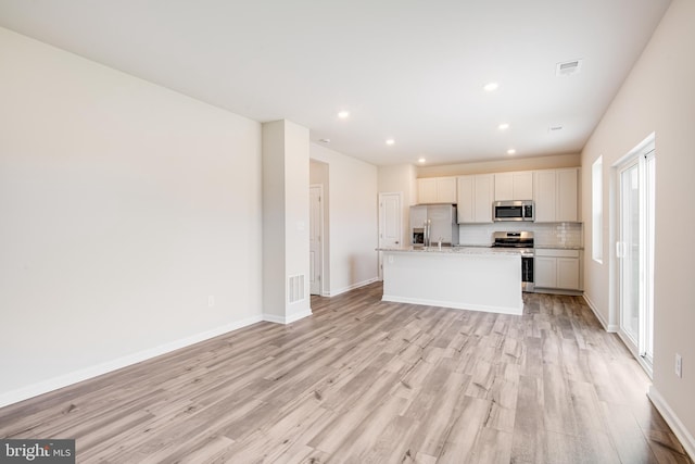 kitchen with light stone countertops, white cabinetry, stainless steel appliances, light hardwood / wood-style flooring, and a kitchen island with sink