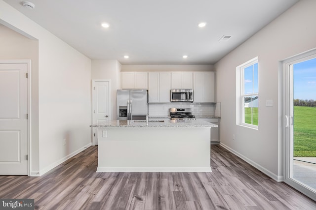 kitchen featuring white cabinets, light stone countertops, an island with sink, and appliances with stainless steel finishes