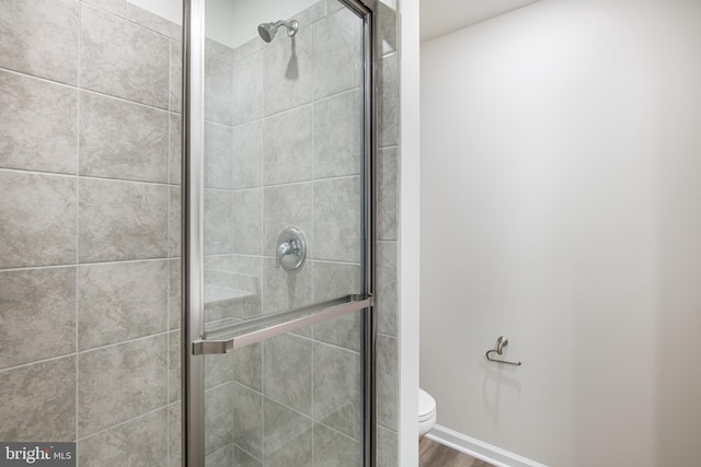 bathroom featuring wood-type flooring, a shower with shower door, and toilet