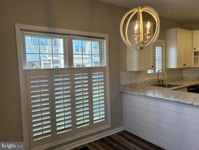 kitchen with pendant lighting, sink, light stone countertops, dark hardwood / wood-style flooring, and white cabinetry