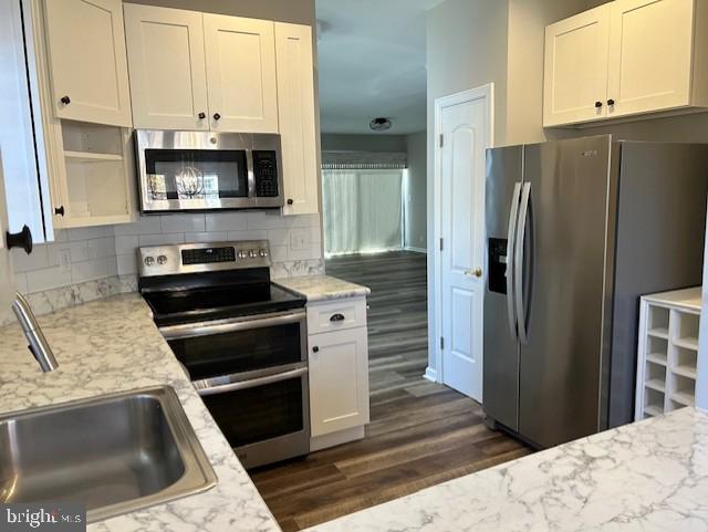 kitchen with sink, dark hardwood / wood-style floors, backsplash, white cabinets, and appliances with stainless steel finishes