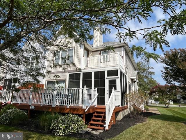 back of property featuring a lawn, a sunroom, and a deck