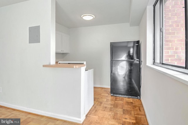 kitchen featuring light parquet flooring, white cabinetry, black fridge, and electric panel