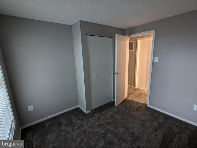 unfurnished bedroom featuring dark colored carpet, a textured ceiling, and a closet