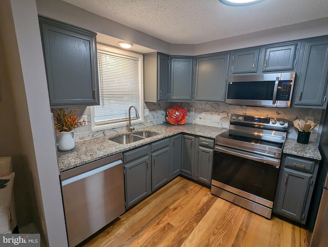 kitchen featuring sink, stainless steel appliances, tasteful backsplash, light stone counters, and light hardwood / wood-style flooring