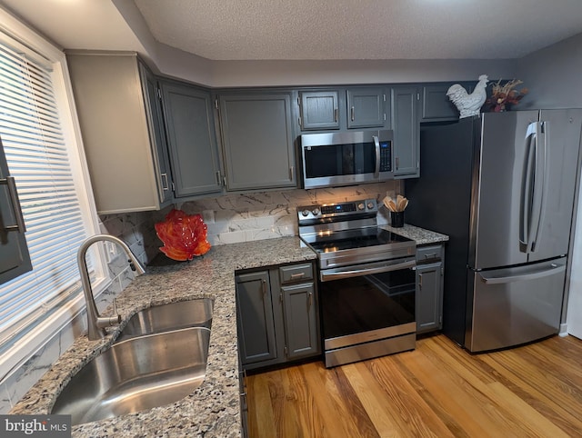 kitchen featuring light hardwood / wood-style floors, light stone countertops, sink, and appliances with stainless steel finishes