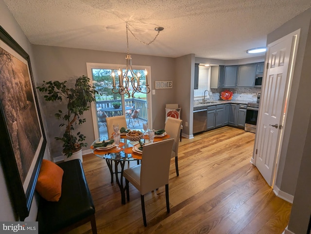 dining room with a textured ceiling, a notable chandelier, light wood-type flooring, and sink