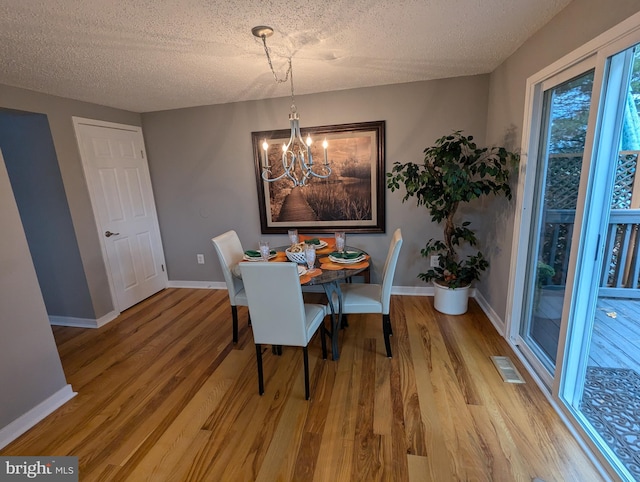 dining room with wood-type flooring, a textured ceiling, and an inviting chandelier