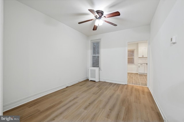 empty room with radiator heating unit, light wood-type flooring, and ceiling fan