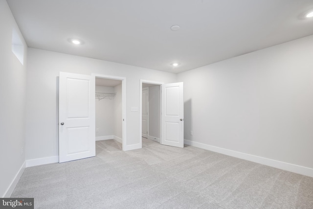 unfurnished bedroom featuring light carpet, a walk in closet, and a closet