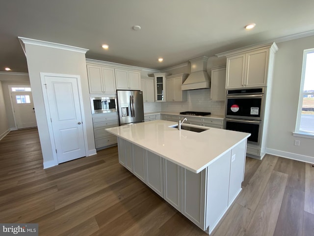 kitchen with a center island with sink, tasteful backsplash, light hardwood / wood-style floors, custom range hood, and stainless steel appliances