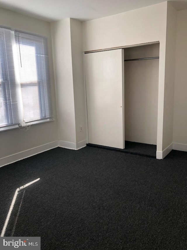 unfurnished bedroom with dark carpet and a closet