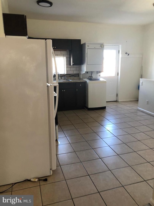 kitchen with tasteful backsplash, sink, white refrigerator, stacked washer and clothes dryer, and light tile patterned flooring